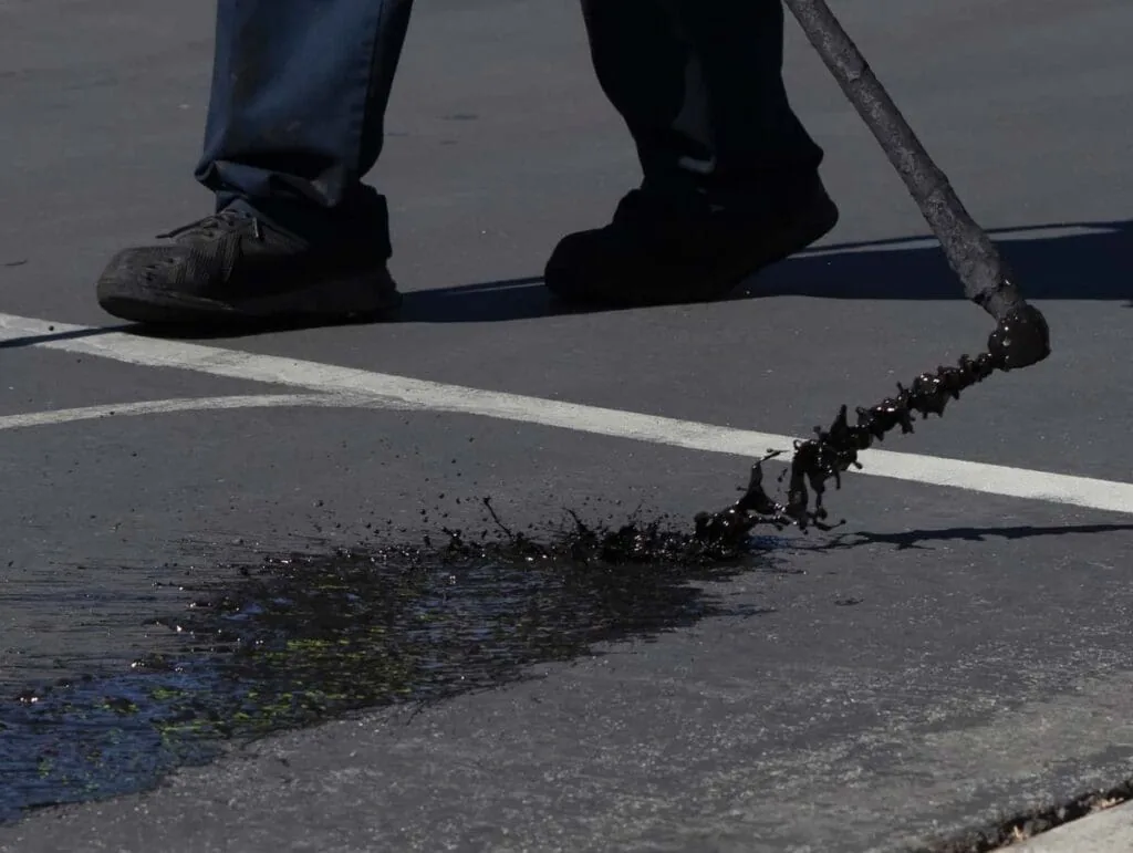 Close-up of a worker spreading sealcoat across an asphalt parking lot