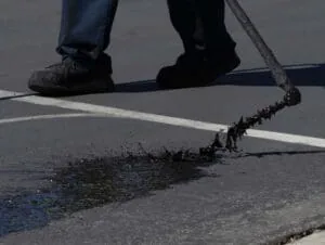 Close-up of a worker spreading sealcoat across an asphalt parking lot