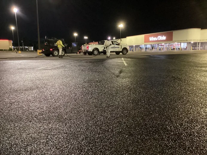 Landmark Paving sealcoating contractor crew applying fresh asphalt sealcoating to commercial parking lot at night.