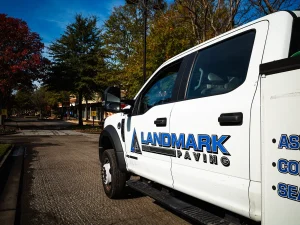 Landmark Paving service truck parked on a residential street with fresh asphalt paving work underway in the background